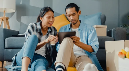 a couple sitting on the floor of their new home shopping for new furniture online